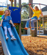 Dos niñas juegan en un tobogán y una red de escalar en un parque vacacional con glamping incluido.