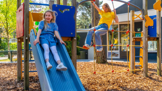 Twee meisjes spelen op een glijbaan en klimnet op een speeltuin bij een vakantiepark met glamping.
