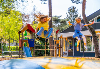 Twee kinderen amuseren zich op een luchtkussen in een vakantiepark met glamping-accommodaties in de natuur.