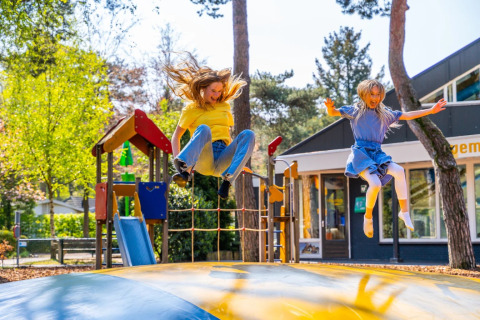 Two children joyfully jump on a large inflatable pillow in a holiday park with glamping accommodations nearby.