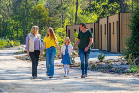A family walks hand in hand along a path at a holiday park with glamping cabins, surrounded by greenery.