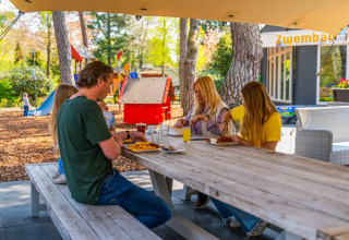 Family enjoying an outdoor meal at a picnic table in a holiday park with playground and glamping options.
