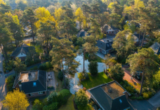 Luchtzicht op een vakantiepark met glamping accommodaties tussen bomen en uitgestrekte natuur.