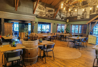 Gezellig restaurant met houten vloer, wijnvatdecor en wandfoto’s in een glamping vakantiepark.