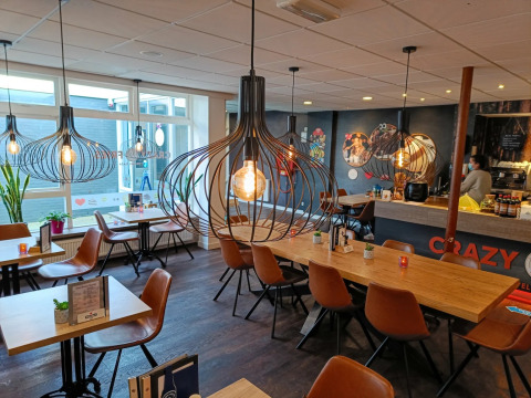 Gezellige café in een vakantiepark met designlampen, houten tafels en leren stoelen voor glampinggasten.