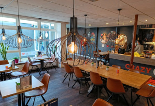 Gezellige eetruimte in een vakantiepark met trendy verlichting, houten tafels en stoelen voor glampingbezoekers.