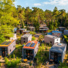 Aerial view of a holiday park with glamping cabins surrounded by lush green trees and natural paths.