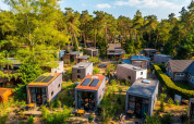 Luchtfoto van een vakantiepark met glampingaccommodaties omringd door bomen en natuurlijke paden.