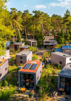 Luchtfoto van een vakantiepark met glampingaccommodaties omringd door bomen en natuurlijke paden.