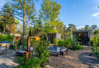 Billedet viser luksuriøse glamping-hytter i en feriepark omgivet af grønne træer og afslapningsområder.