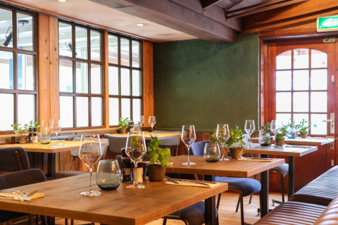 Gezellig restaurant met houten tafels en planten in een vakantiepark dat glamping accommodaties biedt.