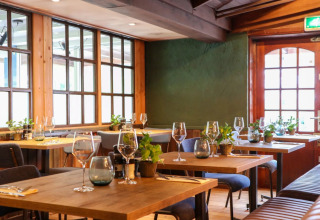 Sfeervol restaurant met houten tafels en planten in een vakantiepark met glamping accommodaties.