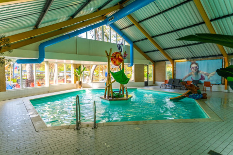 Piscina cubierta con áreas infantiles en un parque vacacional que ofrece alojamiento glamping en la naturaleza.
