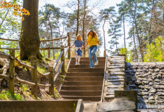 Een vrouw en een kind rennen een trap af in een bosrijk vakantiepark met glamping accommodaties.