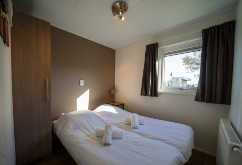 Gemütliches Schlafzimmer in einer Lodge mit zwei Einzelbetten, braunem Schrank und Fenster mit Vorhängen.