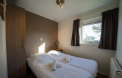 Habitación acogedora en una cabaña con dos camas individuales, sábanas blancas y ventana con cortinas oscuras.