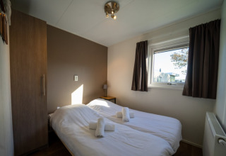 Gemütliches Schlafzimmer in einer Lodge mit zwei Einzelbetten, braunem Schrank und Fenster mit Vorhängen.