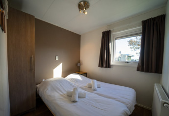 Chambre confortable d’un lodge avec deux lits simples, draps blancs, armoire et fenêtre avec rideaux bruns.