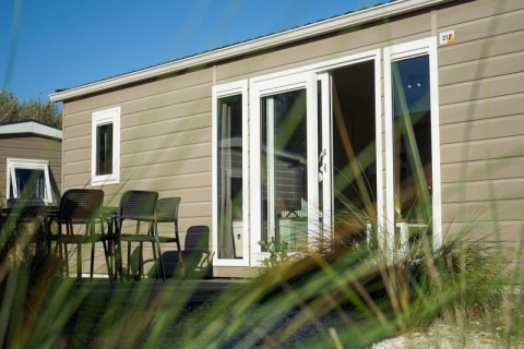 Cabaña moderna con terraza y muebles de exterior vista a través del césped en un día soleado.