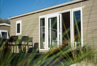 Cabaña moderna con terraza y muebles de exterior vista a través del césped en un día soleado.
