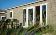 Modern lodge cabin with patio and outdoor furniture, seen through grass, on a bright sunny day.