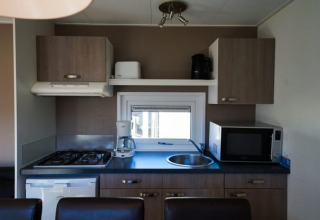 Pequeña cocina en un lodge con estufa de gas, nevera, microondas, fregadero y armarios superiores.