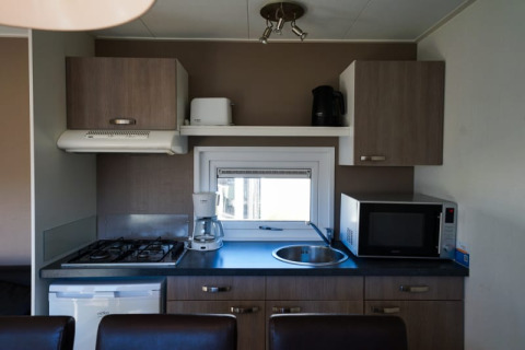 Pequeña cocina en un lodge con estufa de gas, nevera, microondas, fregadero y armarios superiores.