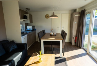 Vista interior de una moderna cabaña con cocina, mesa de comedor, sofá y grandes ventanas luminosas.