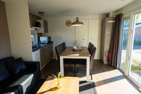 Innenaufnahme einer modernen Lodge mit Küche, Esstisch, Sofa und großen Fenstern mit Tageslicht.