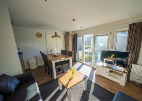 Heller Wohnbereich einer Lodge mit Esstisch, Sofa, Fernseher, großen Fenstern und Gartenausblick.