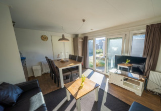 Heller Wohnbereich einer Lodge mit Esstisch, Sofa, Fernseher, großen Fenstern und Gartenausblick.