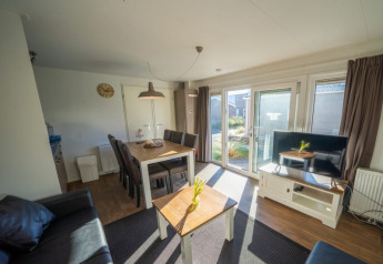 Bright lodge living area with dining table, sofa, TV, large windows, and a view into the garden outside.