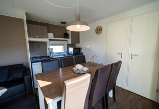 Comedor y cocina americana en una cabaña con sillas marrones, mesa de madera y electrodomésticos modernos.