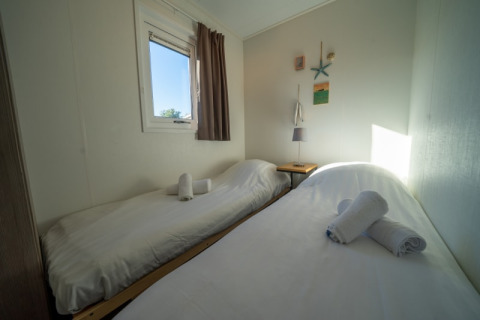 Habitación de alojamiento sencilla con dos camas individuales, sábanas blancas y toallas enrolladas.