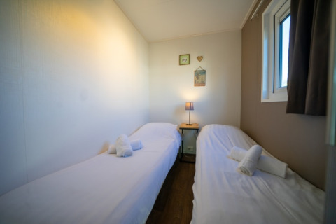 Ein gemütliches Zimmer in einer Lodge mit zwei Einzelbetten, weißen Laken, Handtüchern und einer Lampe.