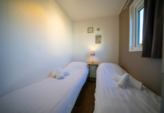 Habitación acogedora en una casa de campo con dos camas individuales, sábanas blancas y una lámpara.