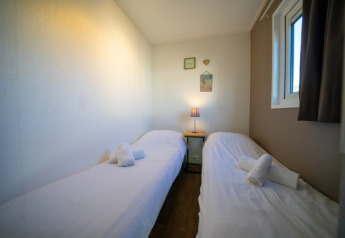 Cozy lodge room with two single beds, white linens, rolled towels, a lamp, and wall decorations.