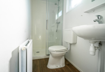 Photo of a modern bathroom at a lodge with a shower cabin, toilet, and sink, all on a wooden floor.