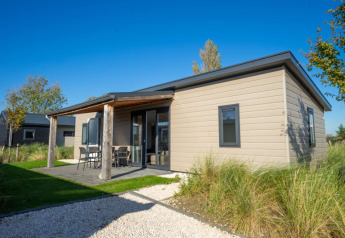 Afbeelding van een moderne lodge met overdekt terras, tuinmeubelen en groen onder een blauwe hemel.