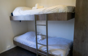 Habitación de lodge con literas de madera, sábanas blancas y toallas enrolladas, ambiente sencillo y cómodo.