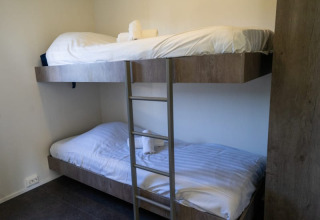 Værelse på en lodge med køjesenge i træ, hvide lagner og håndklæder på hver seng, enkelt og hyggeligt.