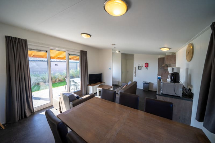 Lodge moderno con mesa de comedor, sofás, zona de cocina y grandes ventanales hacia el jardín.