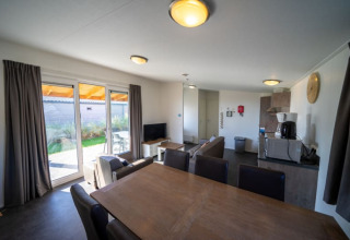 Moderne lodge met eettafel, zithoek, kitchenette en grote ramen die uitkomen op de tuin.