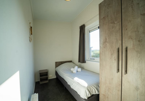 Kleines, helles Einzelzimmer in einer Lodge mit Einzelbett, Fenster, Kleiderschrank und Nachttisch.