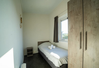 Knusse, lichte eenpersoonskamer in een lodge met enkel bed, raam, kast en nachttafel met handdoeken.