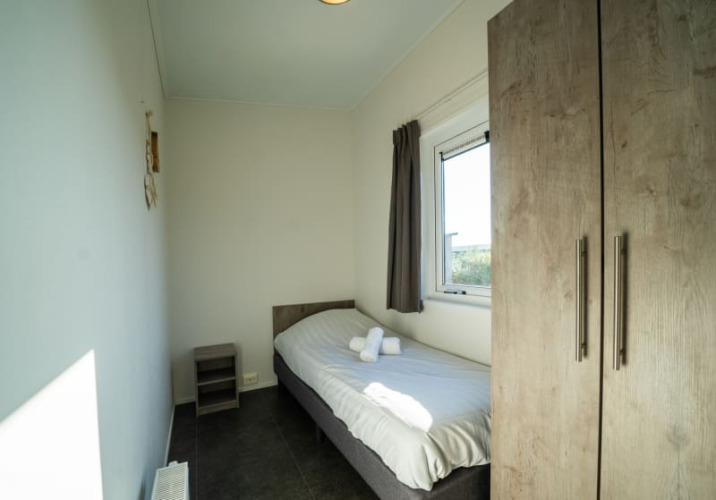 Small, bright single room at a lodge with a single bed, window, wardrobe, and bedside table with towels.