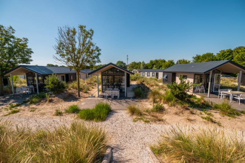 A photo of modern lodges with terraces, surrounded by sandy vegetation and greenery under a clear sky.