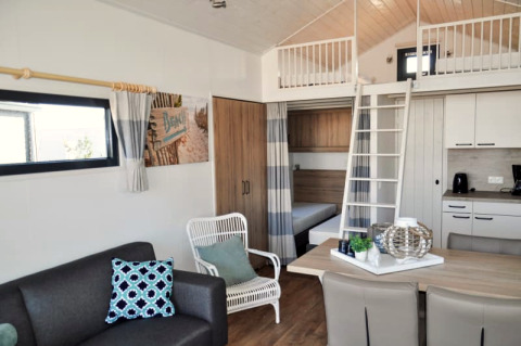Modernes Lodge-Interieur mit Schlafboden, Sitzbereich, Esstisch und Küchenzeile in hellen Farben.