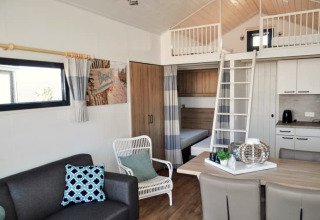 Modernes Lodge-Interieur mit Schlafboden, Sitzbereich, Esstisch und Küchenzeile in hellen Farben.