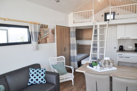 Modern lodge interior featuring a loft bed, kitchenette, dining area, couch, and bright contemporary decor.